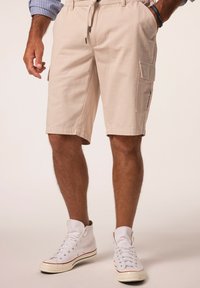 Beige cargo shorts lavet af bomuld, med en snor i taljen, sidelommer og en afslappet pasform. Bæres med hvide høje sneakers.