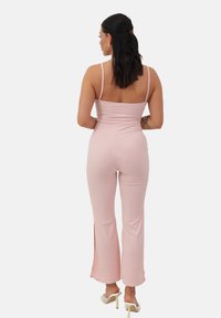 Mono rosa claro con un corsé ajustado y pantalones acampanados que presentan aberturas laterales. Las tirantes finos y la textura acanalada realzan el diseño.