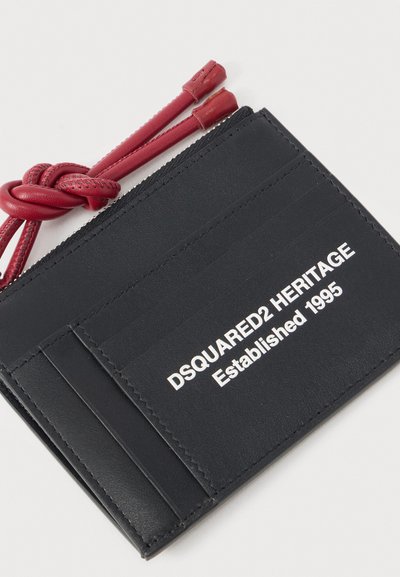 Μαύρος δερμάτινος κάτοχος καρτών με λευκό κείμενο "DSQUARED2 HERITAGE Established 1995" και κόκκινες δερμάτινες κορδόνες φερμουάρ, δεμένες στον κόμπο στο τέλος.