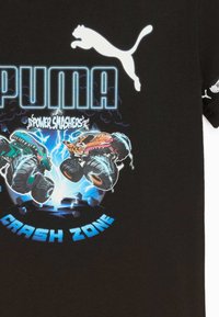Puma logo ar diviem monstru kravas automobiļiem gaisā, zibens efekti un teksts "Power Smashers" un "Crash Zone" uz melnas auduma.
