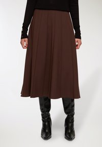 Gonna pieghettata marrone realizzata in tessuto liscio, con spacchi sull'orlo, abbinata a stivali neri al ginocchio, con bottoni sulle maniche del maglione.