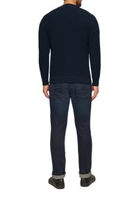 Pull en maille texturée bleu marine avec manches longues et poignets côtelés, associé à un jean en denim foncé et des chaussures noires, vue de l'arrière.