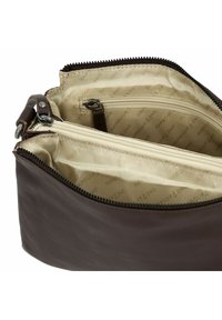 Interno di una borsa in pelle marrone con fodera in tessuto crema, molteplici scomparti e una tasca con zip. Presenta una texture liscia e un design minimalista.