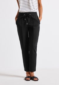 Svarta stretchbyxor med dragsko i midjan, veckad front, sidofickor och tapered ben-design, tillsammans med en randig topp.