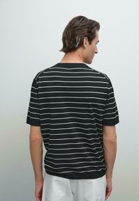Sort kortærmet t-shirt med hvide vandrette striber, rund halsudskæring og afslappet pasform. Stoffet fremstår blødt med en glat tekstur.
