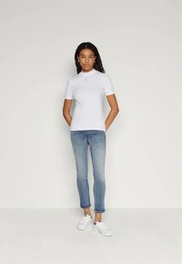 White short-sleeve t-shirt made of cotton, featuring a small logo on the chest. Paired with fitted blue jeans and white sneakers.