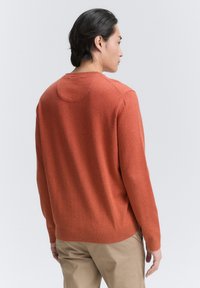 Pull en orange brûlé, fabriqué en tricot, avec un col rond et des manches longues. Dispose de poignets et d'un ourlet côtelés, texture lisse.