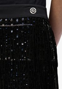Jupe noire en sequins avec franges texturées, dotée d'une taille en satin et d'un détail circulaire en logo argenté sur le devant.
