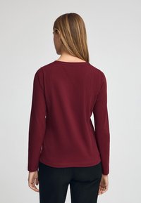 Bordeauxrotes Langarmshirt mit einem Rundhalsausschnitt und figurbetonter Passform. Hergestellt aus weicher Baumwolle, mit glatter Textur und minimalen Details.