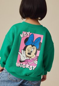 Grøn sweatshirt med et pink grafisk design på ryggen, der viser en tegneseriefigur og teksten "HEY MICKEY." Casual pasform og blød tekstur.