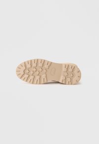 Semelle de chaussure en caoutchouc couleur crème avec un motif de grip texturé et des profondeurs intenses pour l'adhérence. Présente une surface lisse et des bords arrondis.