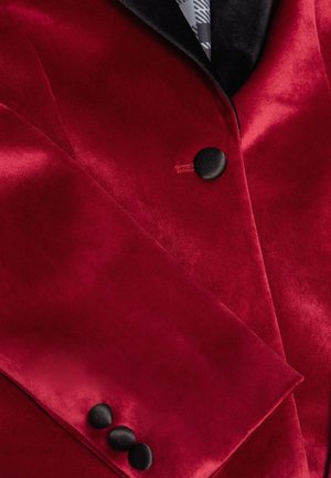 Rode fluwelen blazer met een zwarte sjawlkragen, opvallende zwarte knopen en een%0Agladde textuur met een glanzende afwerking.