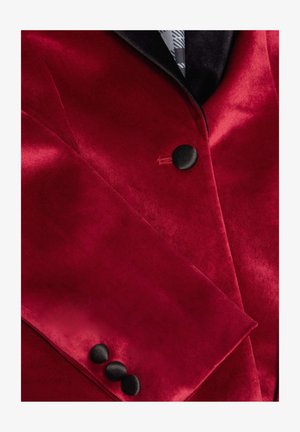 Rode fluwelen blazer met een zwarte sjawlkragen, opvallende zwarte knopen en een%0Agladde textuur met een glanzende afwerking.