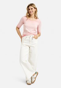 Hellrosa Kurzarmshirt kombiniert mit weißen weiten Hosen und weißen Sneakers mit grünen Akzenten. Einfaches, lässiges Design.