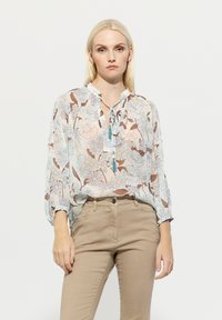 Leichte blumige Bluse mit einer Krawatten-Nackenöffnung, die ein Muster aus blauen und braunen Blumen auf einem hellen Hintergrund zeigt. Lange Ärmel und lockere Passform.