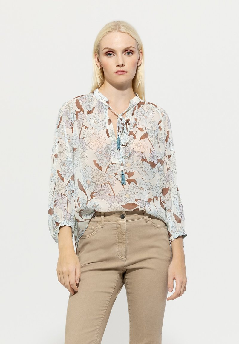 Leichte blumige Bluse mit einer Krawatten-Nackenöffnung, die ein Muster aus blauen und braunen Blumen auf einem hellen Hintergrund zeigt. Lange Ärmel und lockere Passform.