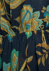 Tmavá látka s květinovým vzorem v tyrkysové, zlaté a olivově zelené barvě s průsvitnou texturou. Elastický pas se staženými detaily a zlatým akcentem ve tvaru "G".