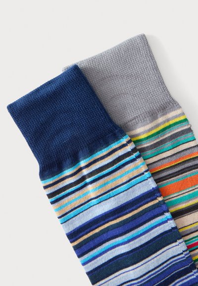 Deux chaussettes pliées avec des motifs rayés ; une chaussette est rayée bleu marine et beige, l'autre est grise avec des rayures vertes, jaunes et orange.