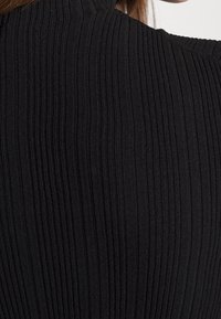 Gros plan sur un tissu en maille côtelée noire sur l'épaule et le haut du dos d'une personne.