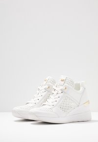 Scarpe da ginnastica bianche con pannelli in rete testurizzata, accenti dorati e tacco a zeppa. Design con lacci e colletto imbottito per il comfort.