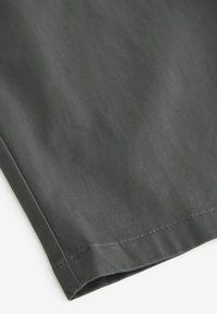 Gros plan sur un ourlet en tissu gris foncé avec des coutures visibles et un bord plié sur un fond blanc.