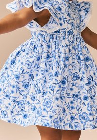 Blaues Blumenkleid mit gesmokten Ärmeln, ausgestattet mit einem weißen Grund und filigranen blauen Blumenmustern. Aus Baumwollmaterial, mit gerafftem Taillendesign.