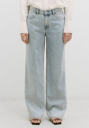 Hellblaue weit geschnittene Jeans aus Denim mit hoher Taille, Fronttaschen und lockerer Passform, kombiniert mit schwarzen Sandalen.