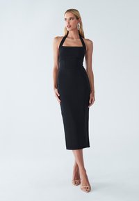 Crna midi haljina s halter izrezom, prilagođenim gornjim dijelom, glatkom teksturom, ravnim suknjom i sandalama na blok petu koje naglašavaju noge.