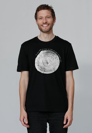 Zwart T-shirt met een zilveren boomring graphic in het midden. Korte mouwen, ronde halslijn, zachte stof en een relaxte pasvorm.