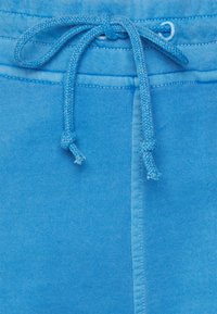 Ceinture de jogging en coton bleu avec cordon de serrage. Texture côtelée avec une couture contrastante le long des bords. Le cordon de serrage se termine par un nœud.