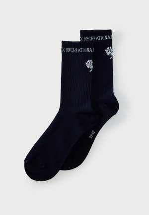 Par de calcetines negros acanalados con texto blanco "RECREATIONAL" en la parte superior y pequeño gráfico de flor blanca en el lateral.