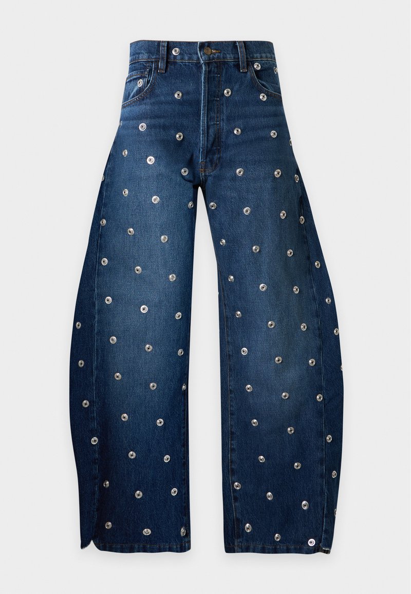 Jean denim bleu foncé à jambes larges avec des œillets métalliques uniformément espacés sur tout le tissu.