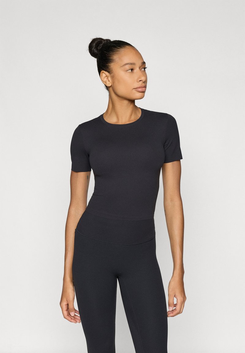 Μαύρο στενό τοπ με κοντά μανίκια από λείο, ελαστικό ύφασμα, συνδυασμένο με αντίστοιχα κολάν υψηλής μέσης, και τα δύο σε μονόχρωμο χρώμα.