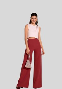 Top corto de color rosa claro combinado con pantalones amplios de color burdeos; la modelo sostiene un bolso de mano plateado texturizado y se encuentra frente a un fondo neutro.