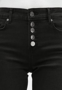 Jeans noirs taille haute avec une fermeture à cinq boutons, en denim robuste, et des poches avant. Texture lisse avec des détails de couture discrets.