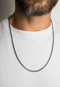 Colier din metal argintiu, cu un design neted și răsucit, așezat pe o cămașă albă, având o grosime medie și un finisaj lustruit.
