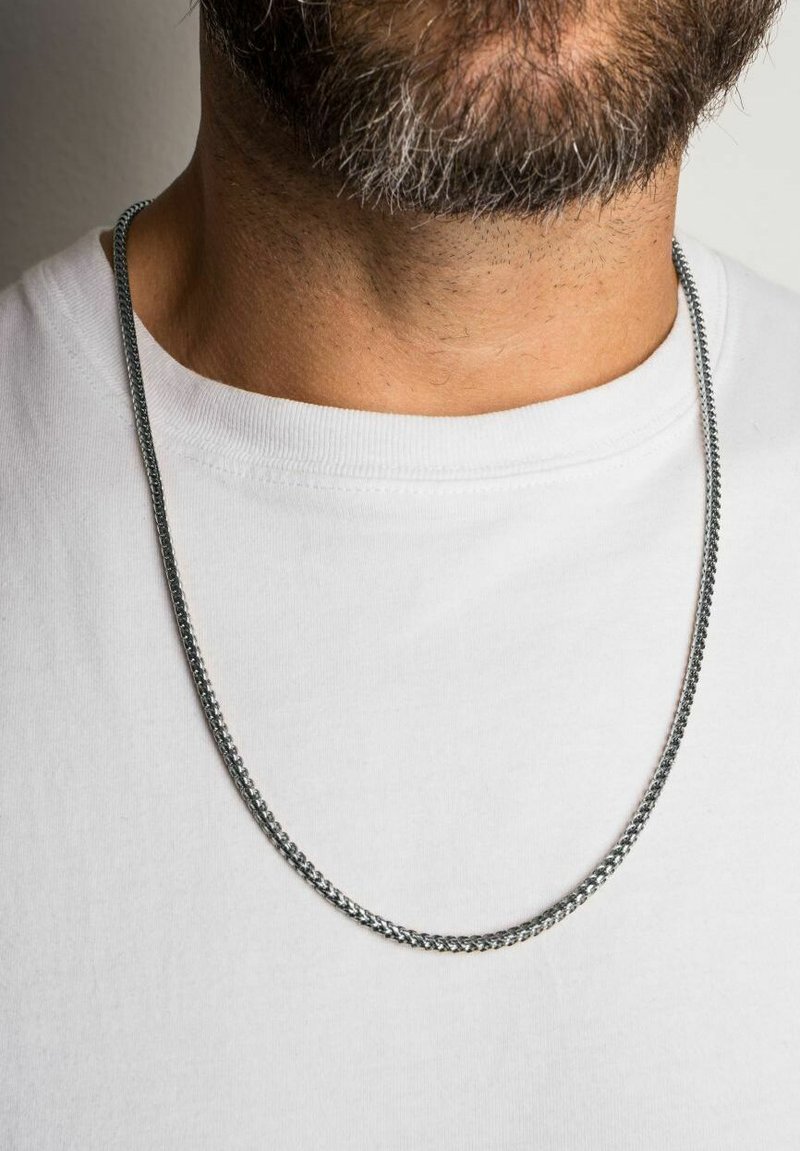 Colier din metal argintiu, cu un design neted și răsucit, așezat pe o cămașă albă, având o grosime medie și un finisaj lustruit.