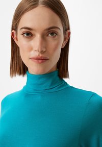 Turkusowy sweter z golfem wykonany z gładkiego, elastycznego materiału. Posiada wysoki kołnierz i długie rękawy, z dopasowanym krojem i bez widocznych wzorów.