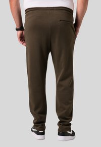 Olijfgroene joggers met een slim fit, elastische tailleband en een detail van een achterzak, gecombineerd met zwart-witte sneakers.