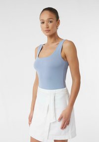 Helleblaue ärmellose Bluse aus geripptem Stoff mit quadratischem Ausschnitt, kombiniert mit einem weißen Wickelrock mit gebundenem Taillenbund.