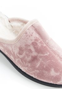 Pantoufle en velours rose avec une texture douce, un design arrondi et une semelle ressemblant à du daim. Présente un dessus à motifs et une bordure beige le long de l'ouverture.