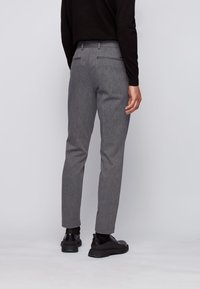 Szare zwężane spodnie z teksturowanym wzorem, z dwoma tylnymi kieszeniami i średnim stanem. Noszone z czarnymi butami i bluzką z długim rękawem.