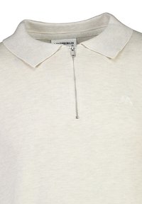 Vaaleanbeige polo-paita, jossa on ribbipinta, vetoketjukaulus ja pieni brodeerattu logo vasemmassa rinnassa.