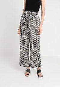 Pantalons à jambes larges en tissu imprimé présentant un motif géométrique en noir, blanc et jaune. Taille à cordon de serrage et matériau léger.