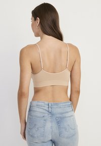 Nøgen bralette med justerbare stropper og glat tekstur, kombineret med lyseblå jeans med syede lommer og detaljer ved linningen.