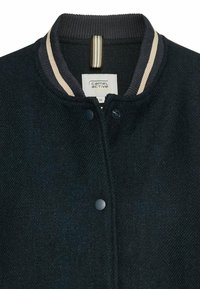 Schwarze Wollmischung Bomberjacke mit geripptem Kragen und beigen Streifen, Druckknöpfen und einem Label am Hals. Strukturierter Stoff.