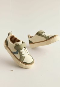 Creme- og olivengrønne sneakers med en lys brun sål, der har hvide snørebånd, en tekstureret tåhætte, og et stribet inderskud.