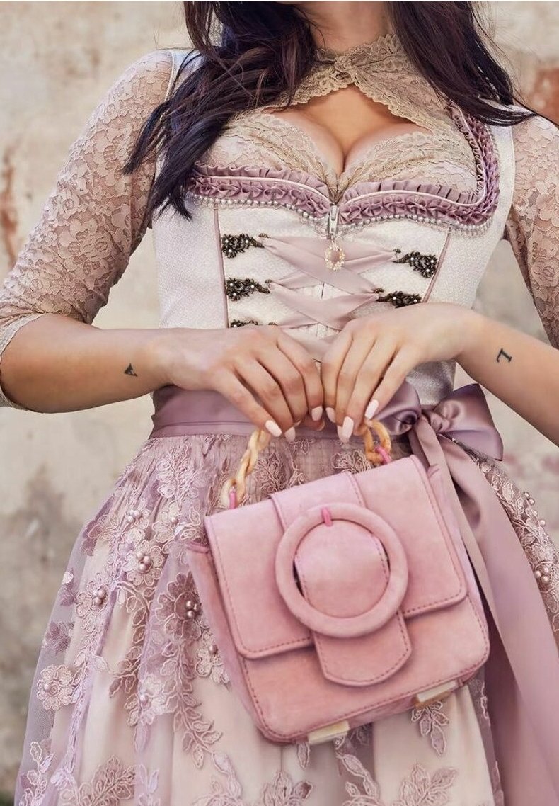 Femme portant une robe en dentelle rose avec des détails de corset, tenant un sac à main rose assorti avec une boucle ronde et des poignées en bois.