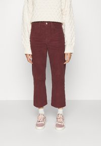Pantalon en velours côtelé bordeaux à coupe droite et longueur raccourcie, associé à un pull tricoté crème et des baskets rose clair.