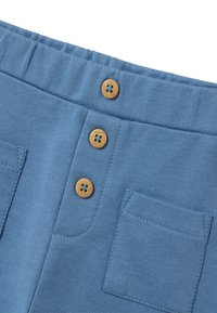 Blauwe katoenen stof met een elastische tailleband, voorzien van drie houten knopen en een patchzak op de voorkant. Gladde textuur, casual ontwerp.